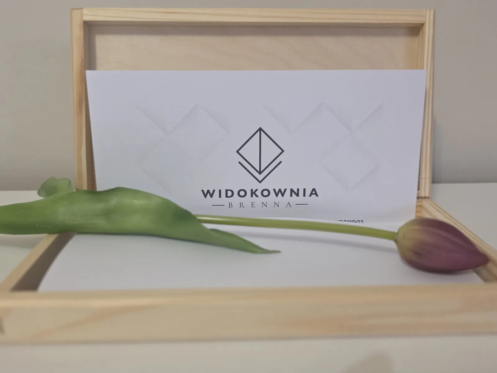 Otwarte drewniane pudełko z voucherem Widokowni i tulipanem